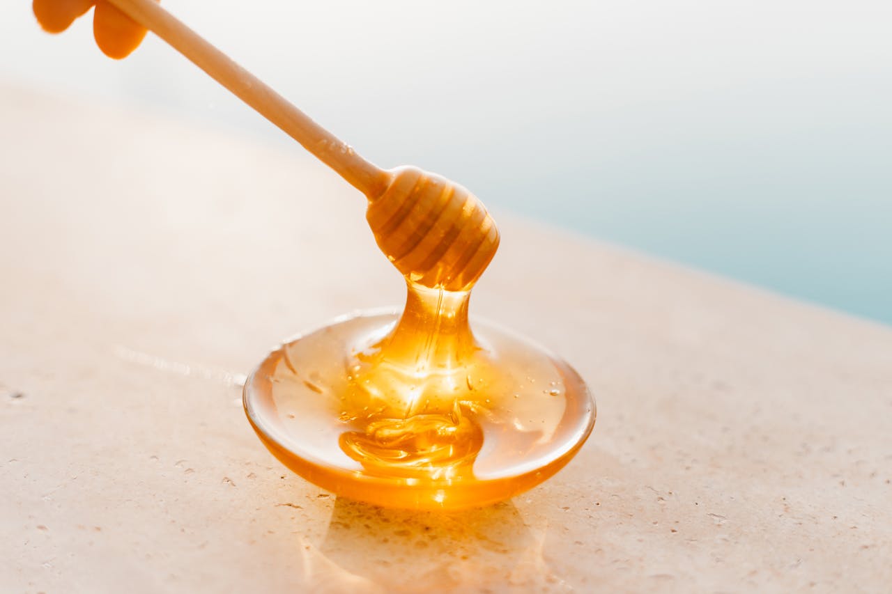 Golden honey flowing from a wooden dipper onto a glass plate, captured in warm daylight.